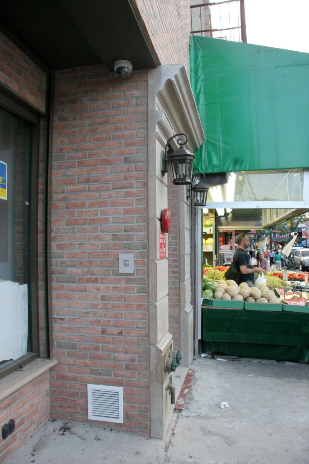 Brick storefront corner beside an outdoor produce stand under a green awning.