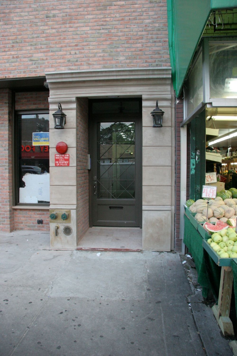 Narrow storefront entrance with a green door beside a produce display on a city sidewalk