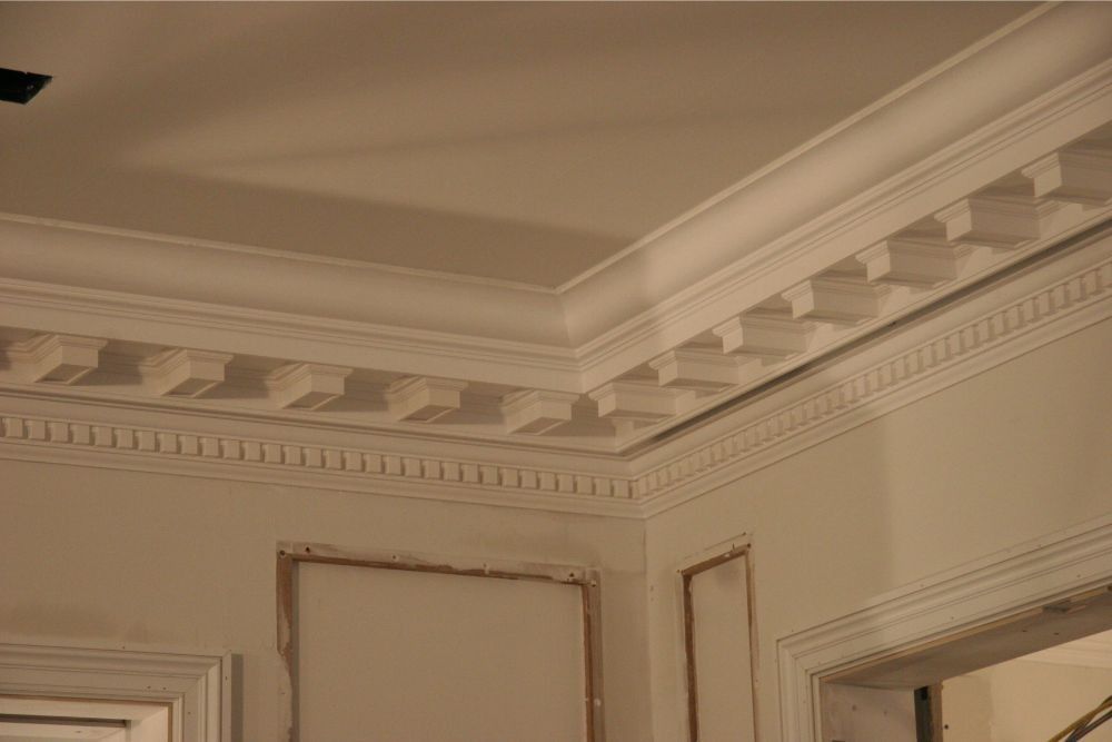 Corner of a cream-colored room with ornate crown molding and decorative ceiling trim