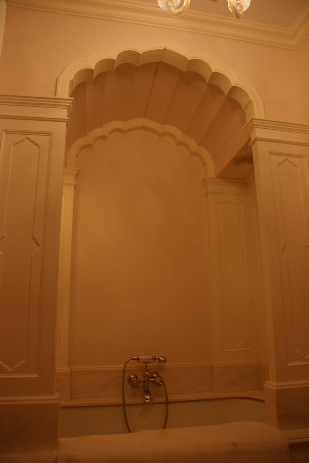 Ornate marble bath alcove with arched niche and chrome faucet, lit in warm amber tones