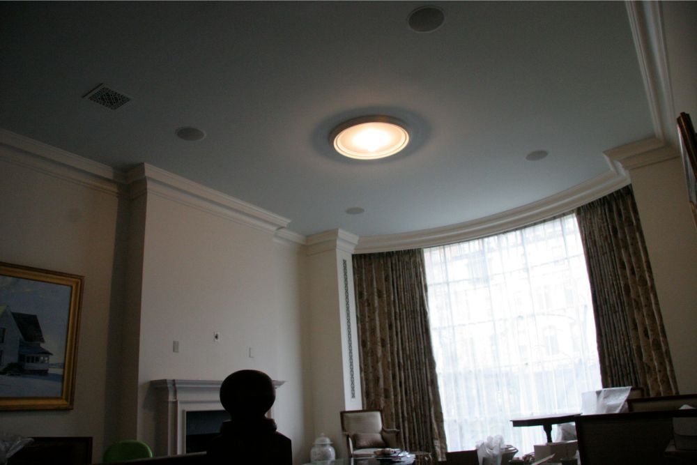 Dim living room with a bright round ceiling light and large bay window with curtains