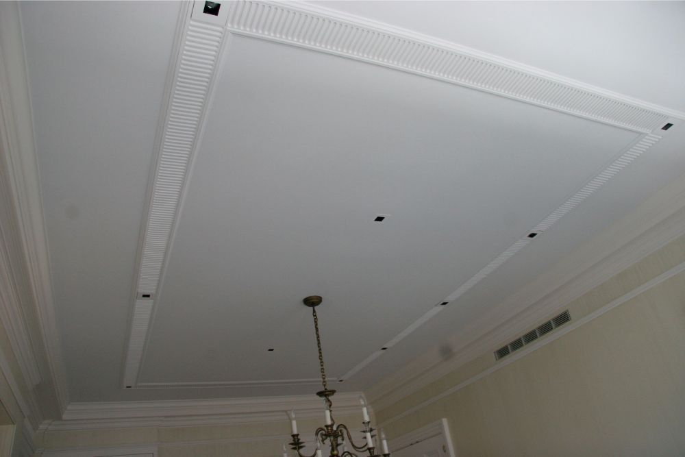 White ornate ceiling with crown molding, recessed panel, hanging light fixture, and small ceiling holes