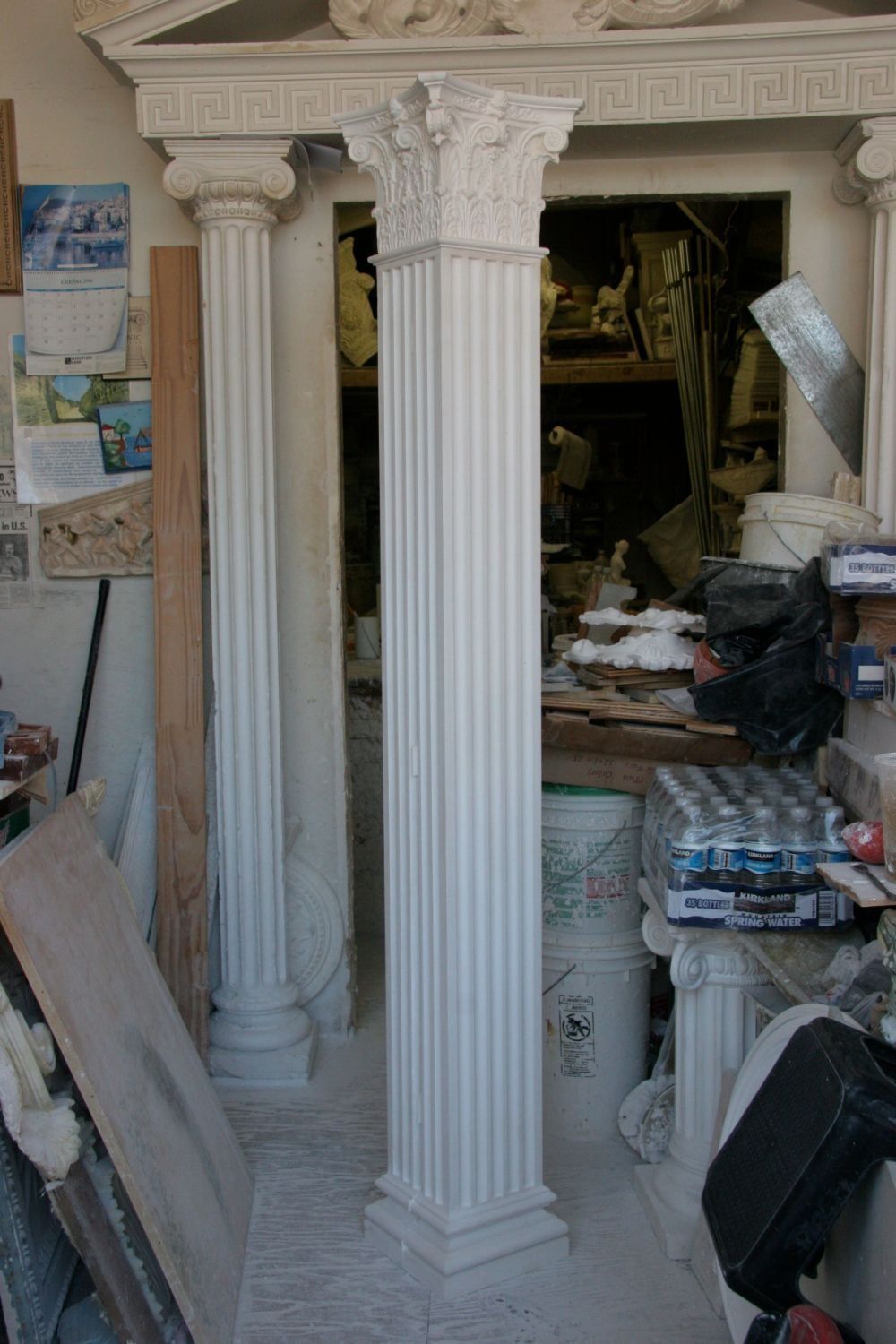 White decorative column in a cluttered interior with shelves, papers, and furniture in the background
