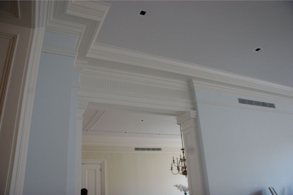 White ornate interior with decorative molding, a doorway, and a hanging chandelier in a bright room