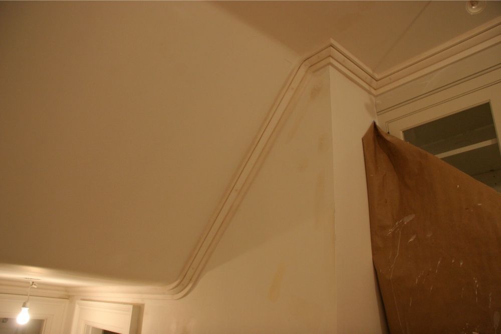 Indoor ceiling corner with crown molding and an open wooden door under warm light