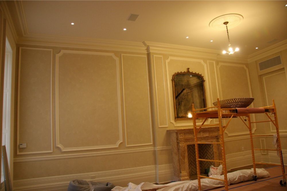 Elegant cream-walled room with decorative molding, a hanging light, and scaffolding covered in cloths
