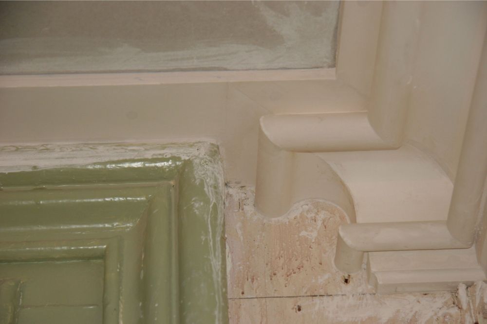 Close-up of a cream-colored architectural molding corner with decorative trim and peeling paint