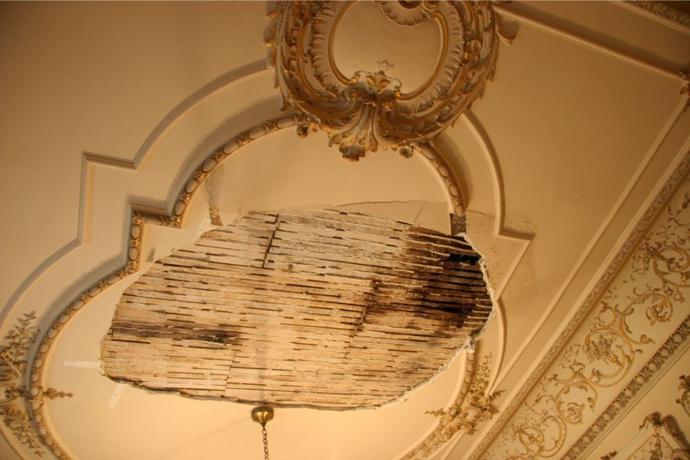 Damaged ceiling panel hanging from ornate plaster ceiling in a historic room