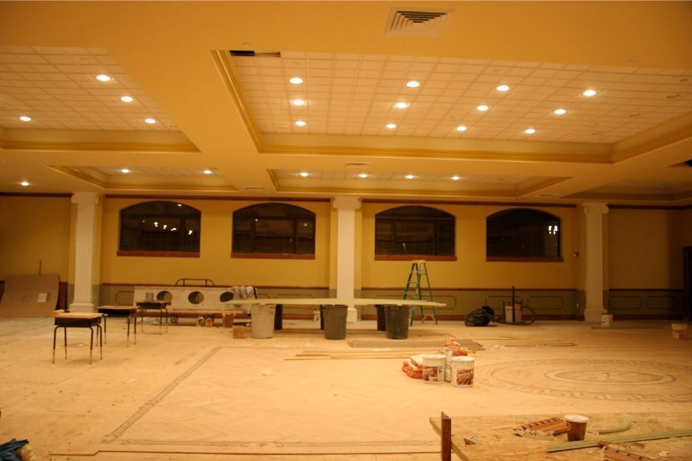 Empty banquet hall under construction with recessed lights, tables, and tools scattered on the floor
