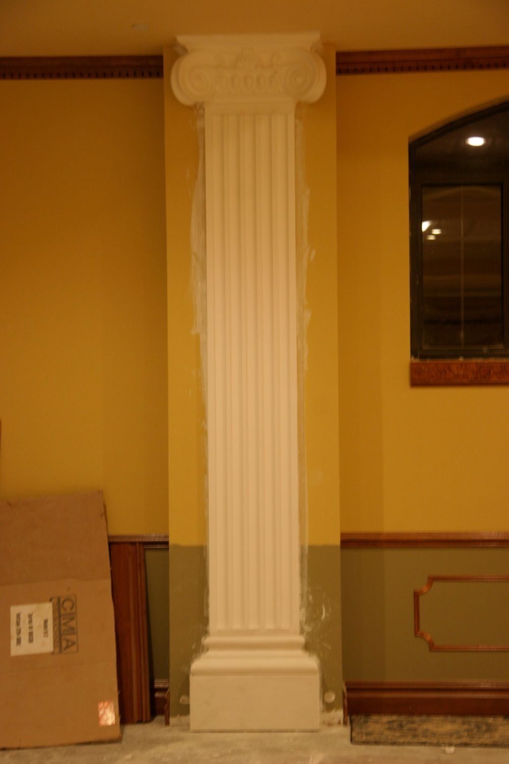 White fluted column in a warmly lit interior beside a window and cardboard box
