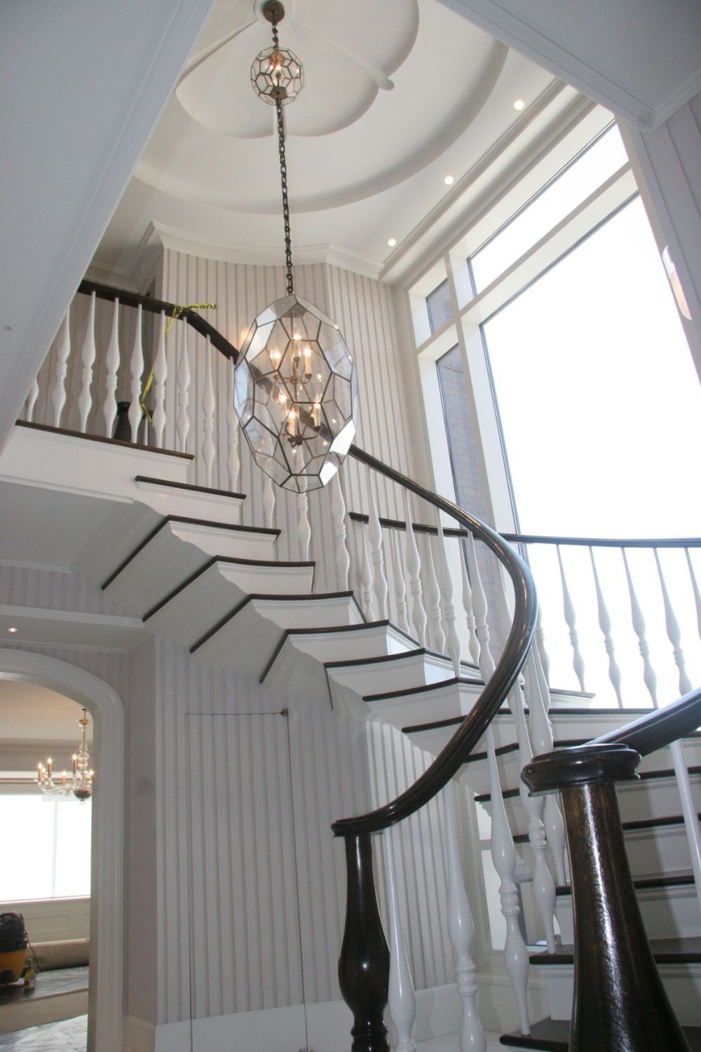 Elegant curved staircase in a bright foyer with white railings and a hanging chandelier
