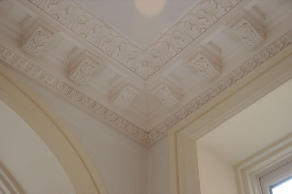Ornate cream-colored ceiling molding and cornice detail near a window and archway