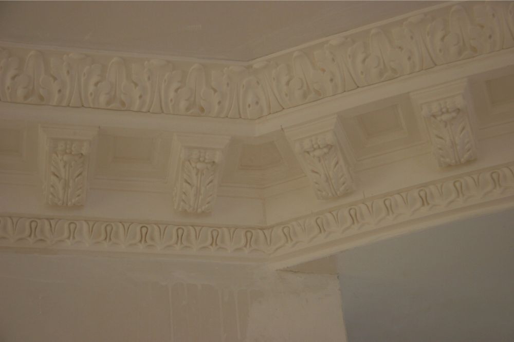 Beige ornate plaster crown molding and ceiling cornice detail in an interior room