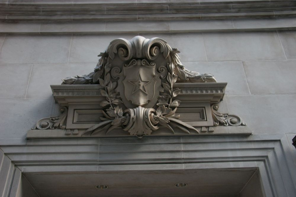 Decorative stone crest above a doorway on a gray building facade