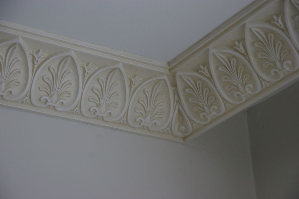 Decorative cream leaf border molding along the top of a gray wall and ceiling corner