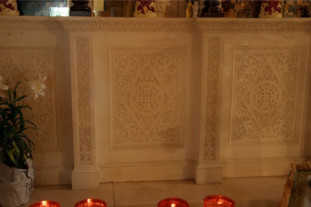 Ornate cream-colored wall panels with carved details, lit by red candles along the bottom edge