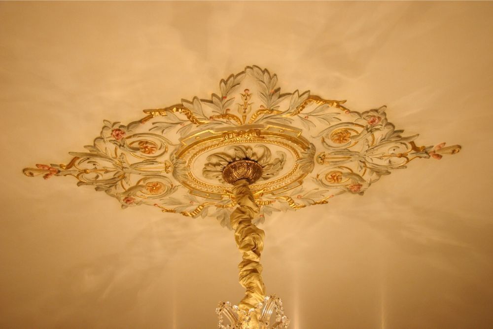 Ornate gold chandelier ceiling medallion with decorative floral details against a warm beige ceiling