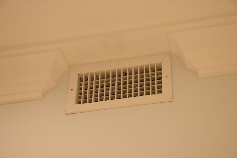 White wall air vent near the ceiling with a beige trim section around it