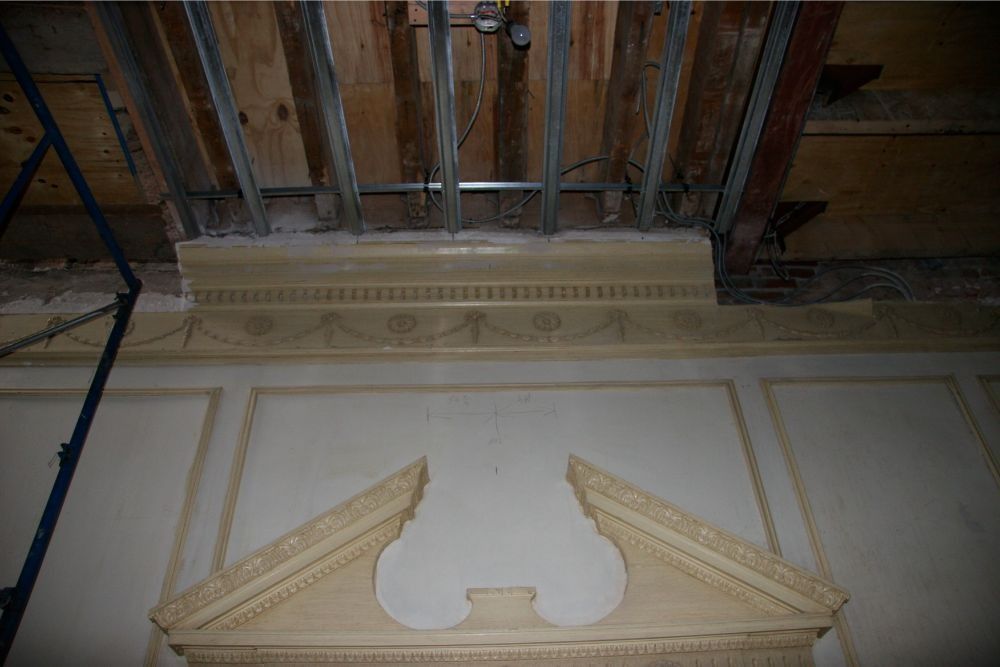 Ornate ceiling and decorative wall molding in a historic interior, with exposed beams above.