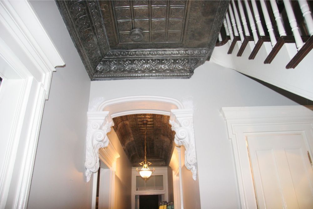 Ornate hallway ceiling with decorative plaster, dark wood panels, and a hanging light fixture