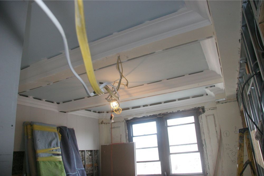 Ceiling with exposed beams, hanging light bulb, and a window in a partially finished room