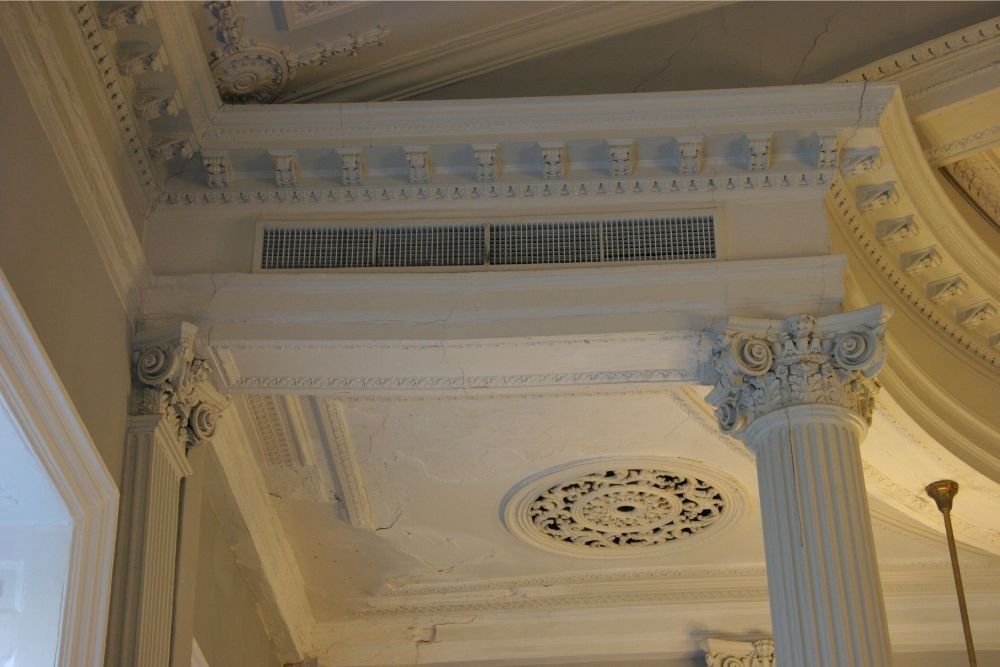 Ornate white ceiling with decorative molding, fluted columns, and a round medallion in a classical interior