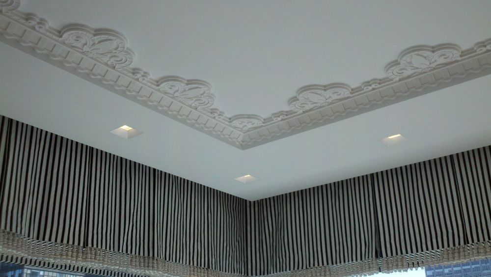 Decorative ceiling corner with ornate molding, recessed lights, and striped curtains below