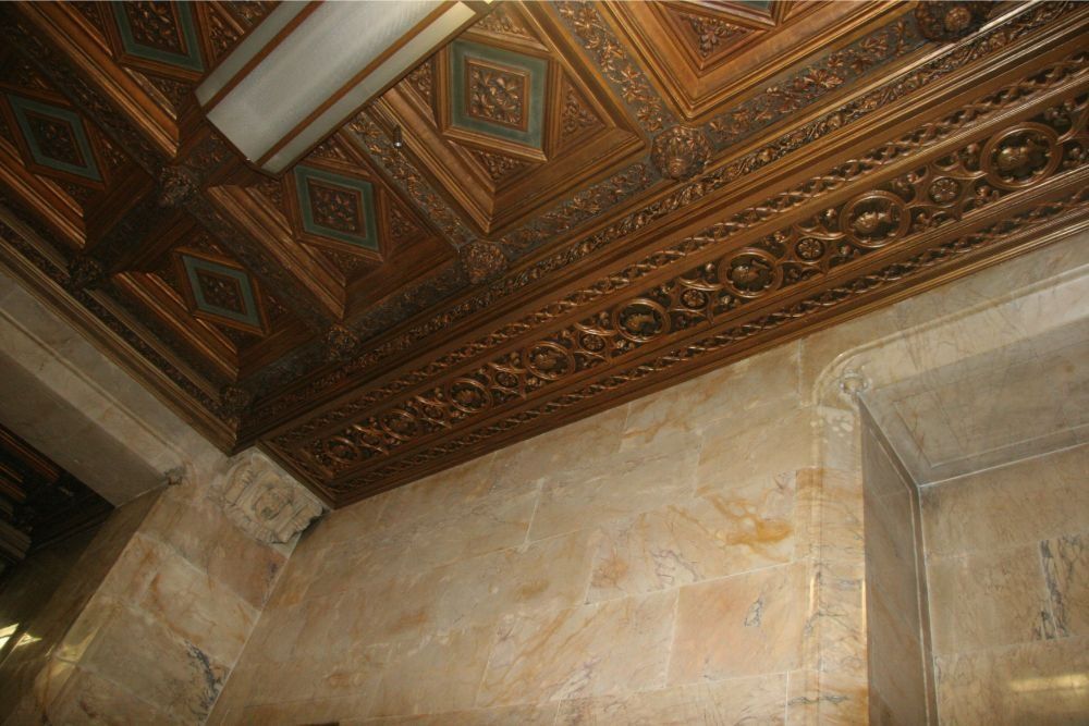 Ornate carved wooden ceiling with geometric patterns above pale stone walls in a historic interior