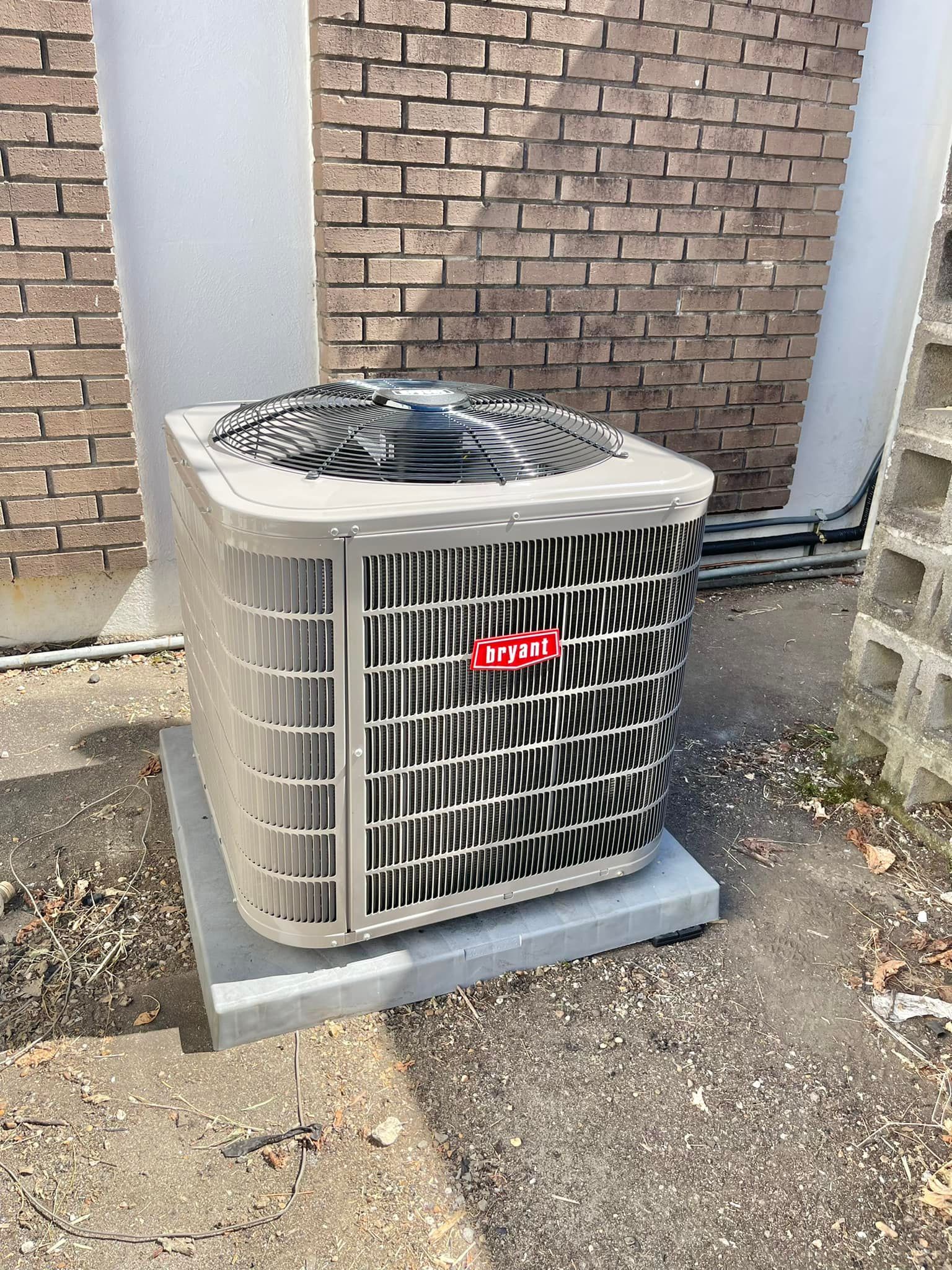 A large air conditioner is sitting on top of a concrete base in front of a brick wall.