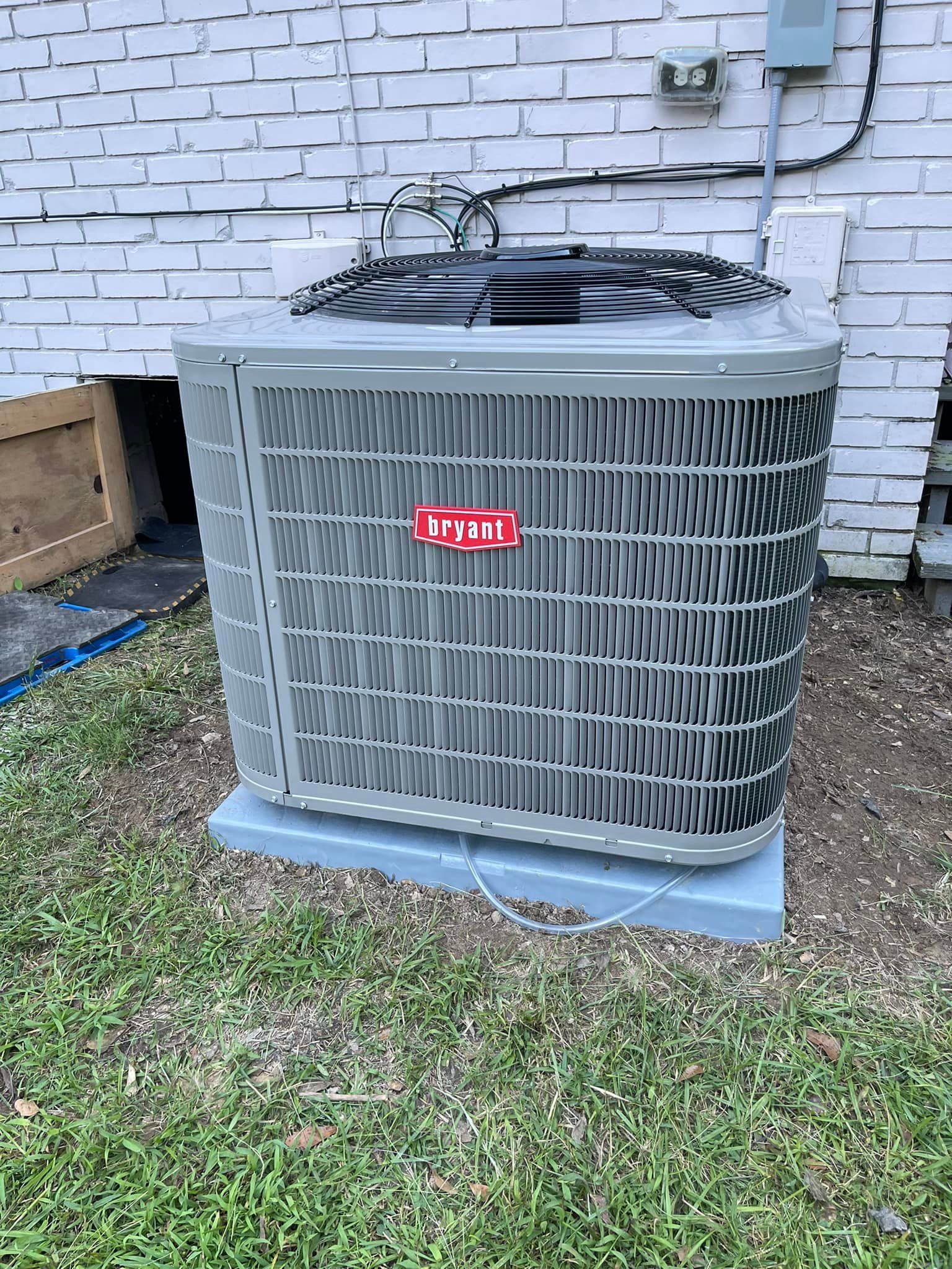 A large air conditioner is sitting in the grass in front of a white brick building.