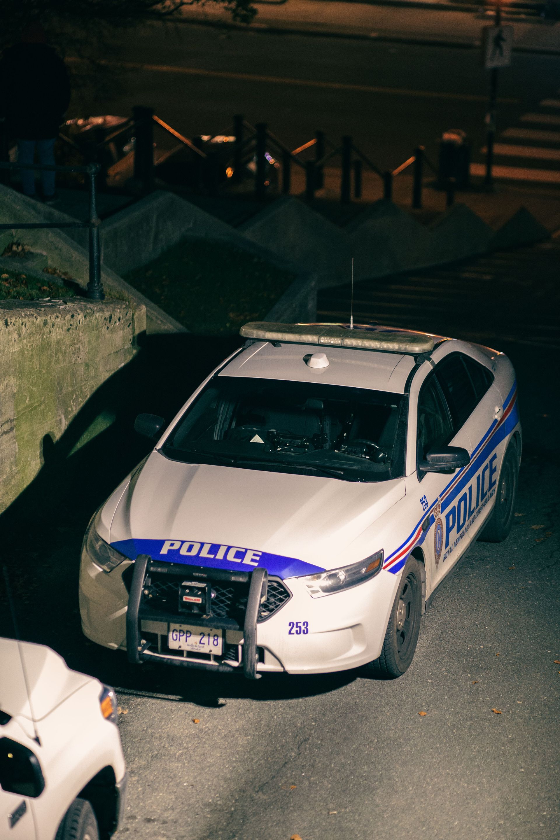 Police car parked at night beside a curb, with blue markings and visible front damage.