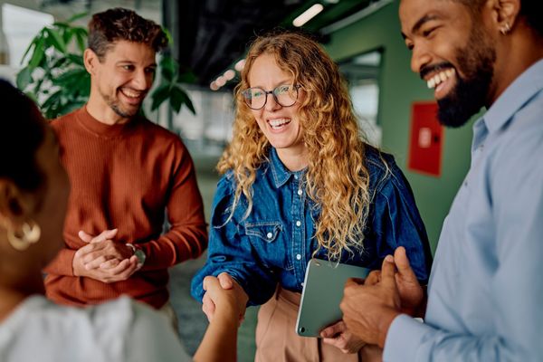 Group of people smiling, shaking hands in a brightly lit office setting. Group of people smiling, shaking hands in a brightly lit office setting.