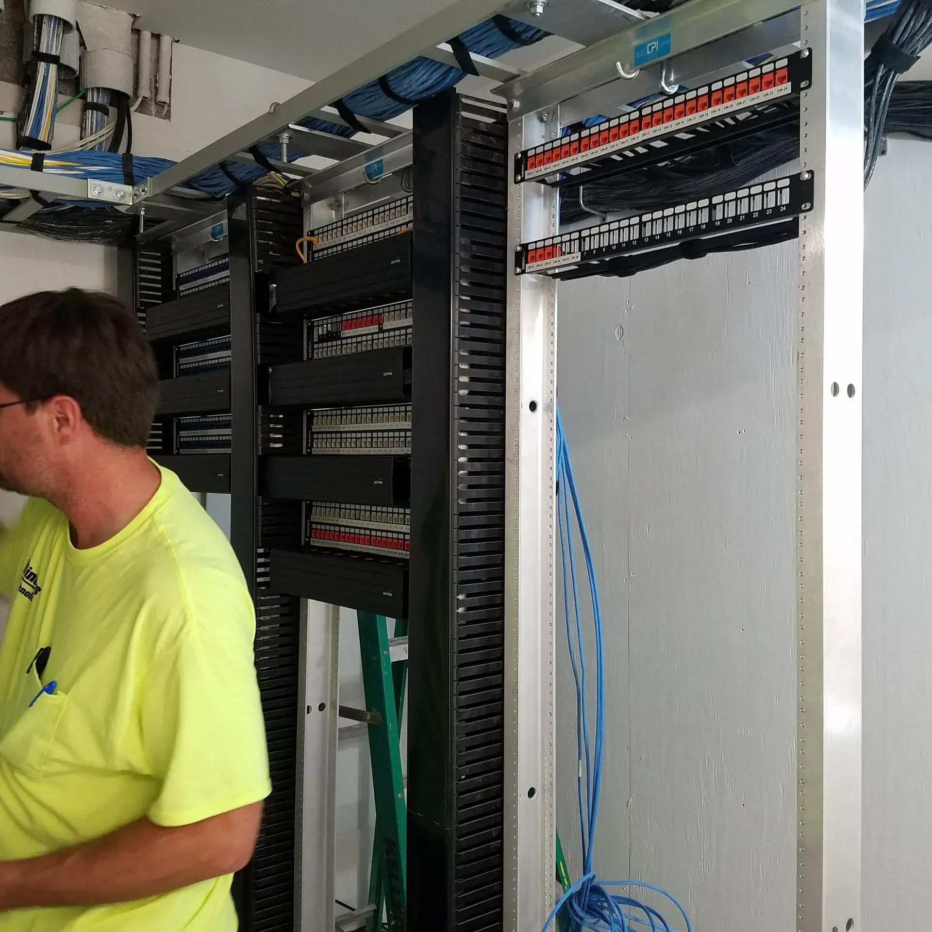 A man in a yellow shirt is standing in front of a server rack