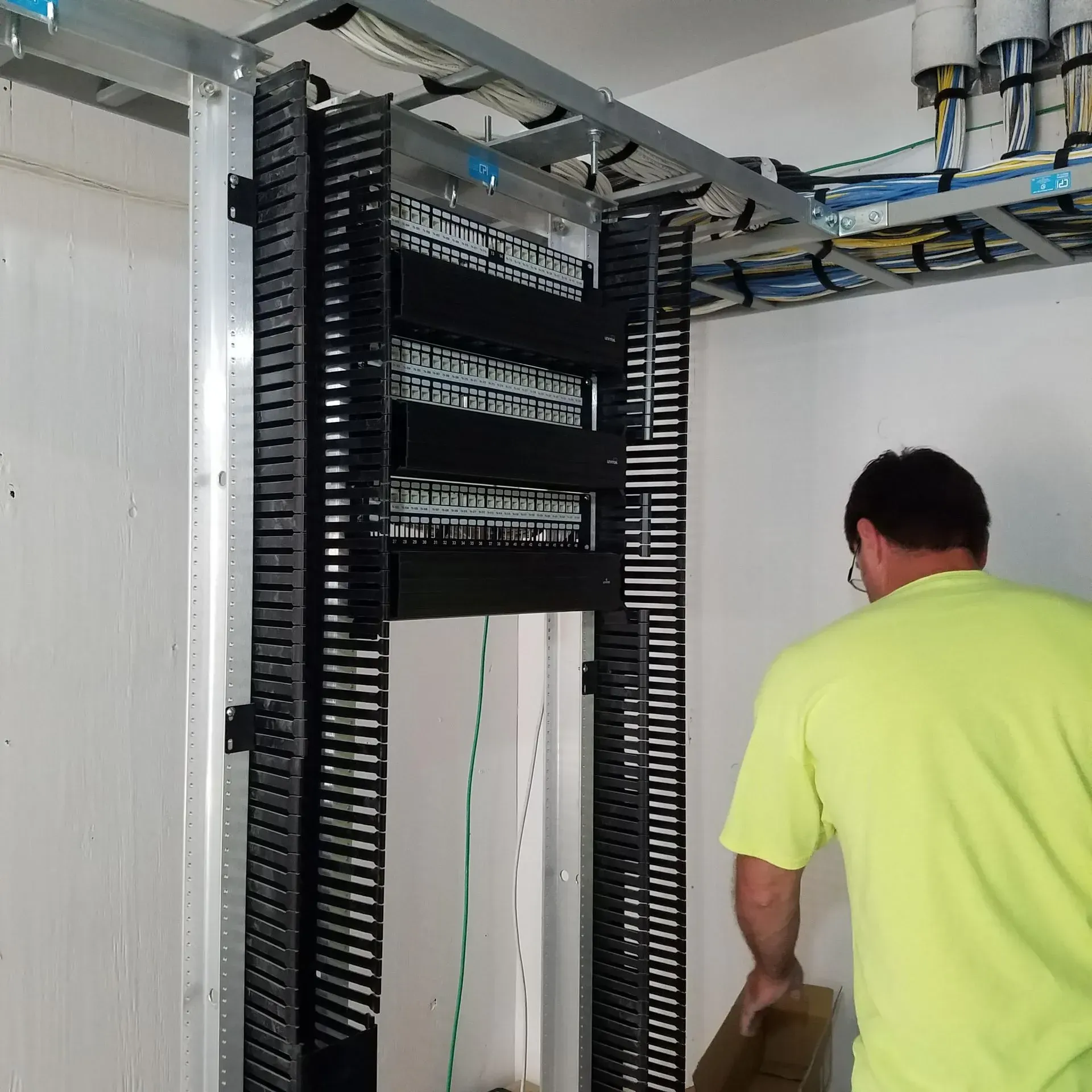 A man in a yellow shirt is working on a server rack