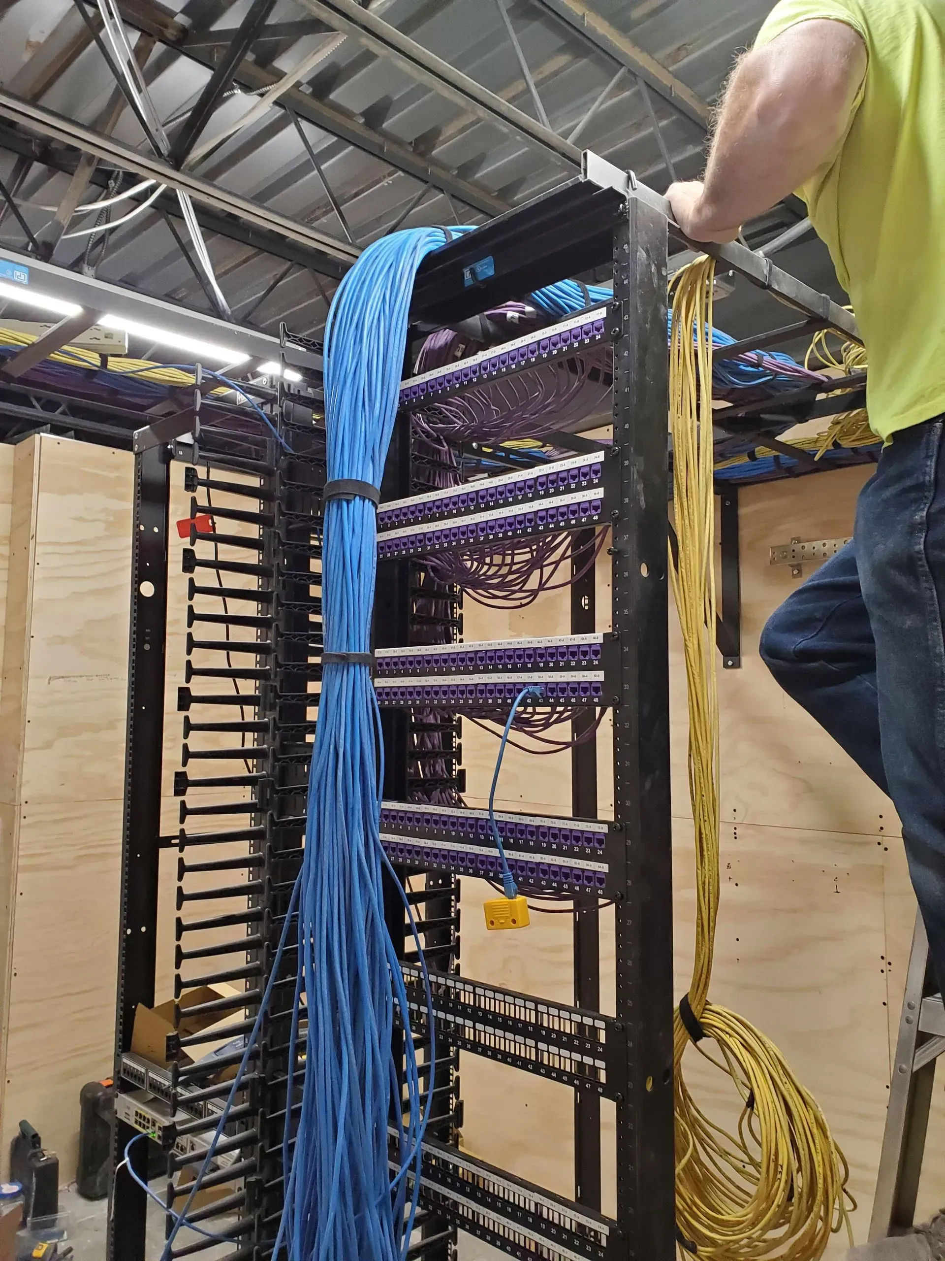 A man in a yellow shirt is working on a server rack