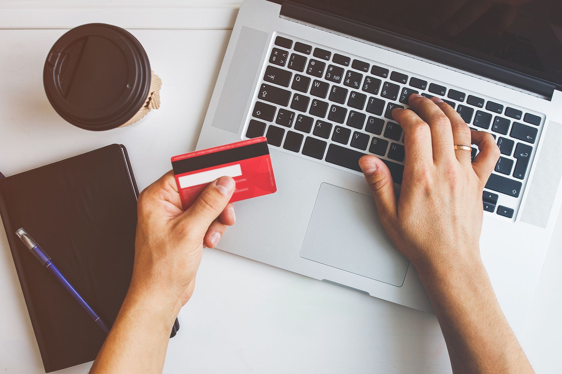 Man Holding a Credit Card While Typing on Laptop