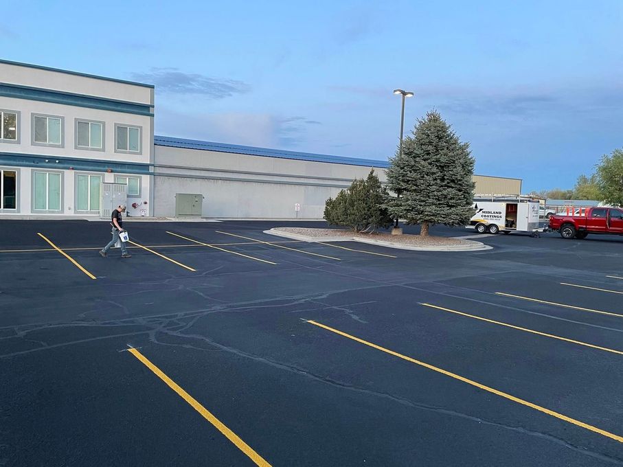 A person walks across a parking lot toward a large commercial building with white walls and blue trim at dusk.