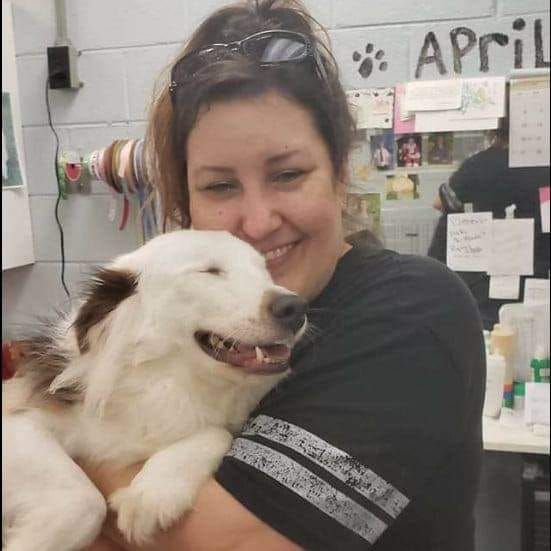 Woman holding a smiling, white and brown dog; smiles and hugs in an animal shelter.