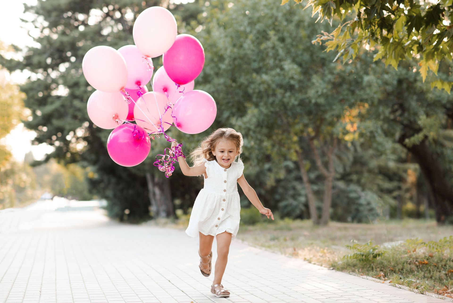 Girl running with pink balloons outdoors.