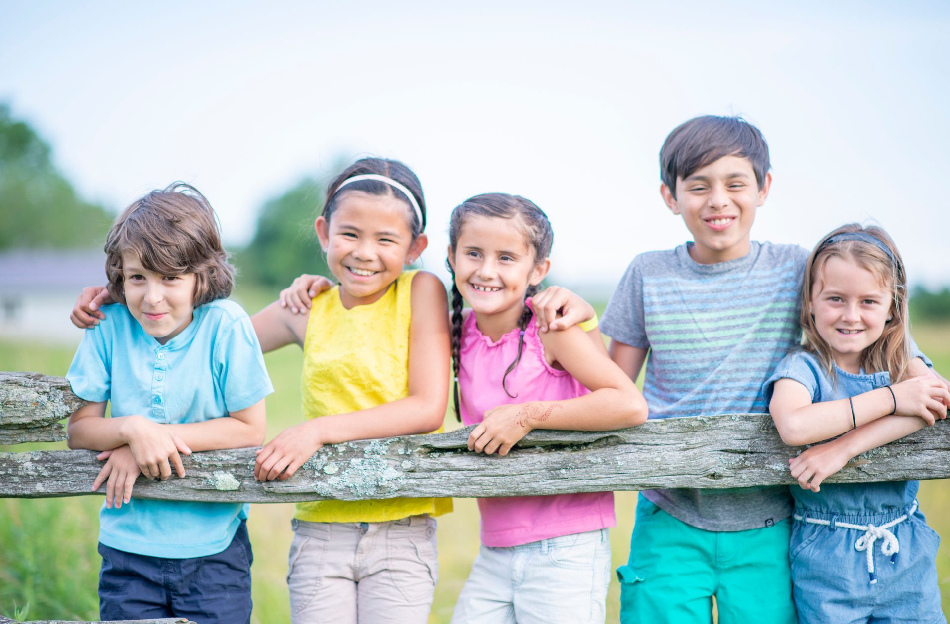 Group of children smiling and posing together behind a weathered wooden fence in an outdoor setting.