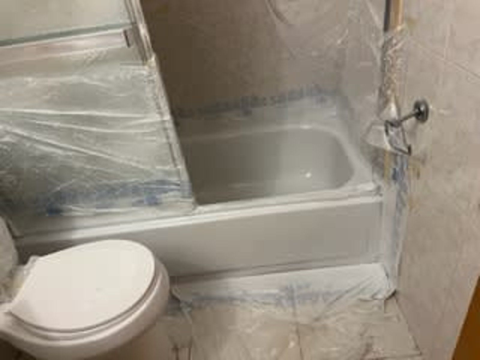 A bathroom with a toilet , tub and shower covered in plastic