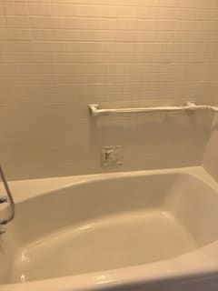 A white bathtub is sitting in a bathroom next to a white tiled wall.