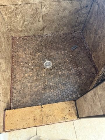 A shower stall with coins on the floor and a drain
