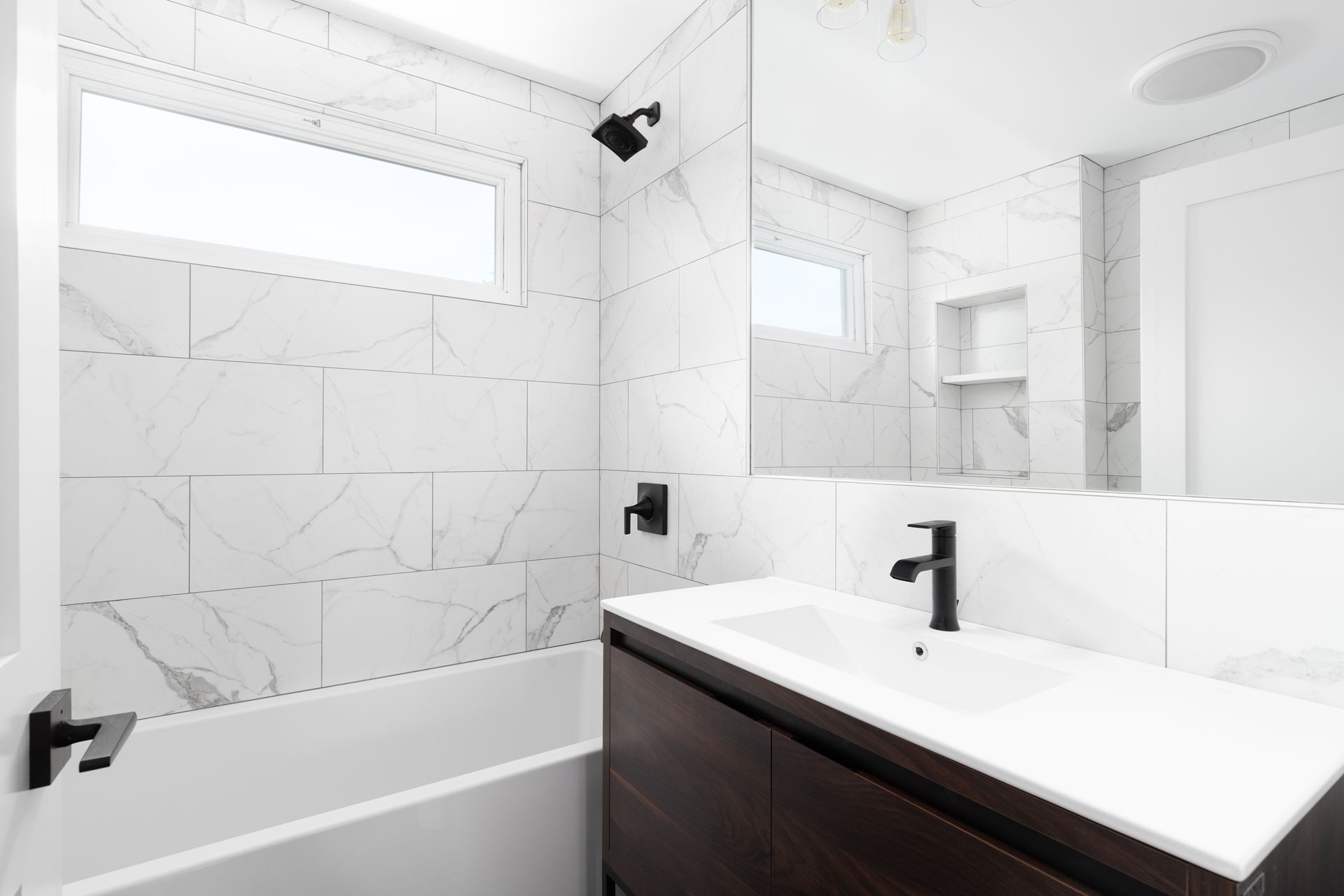 A bathroom with white tiles , a sink , a tub and a mirror