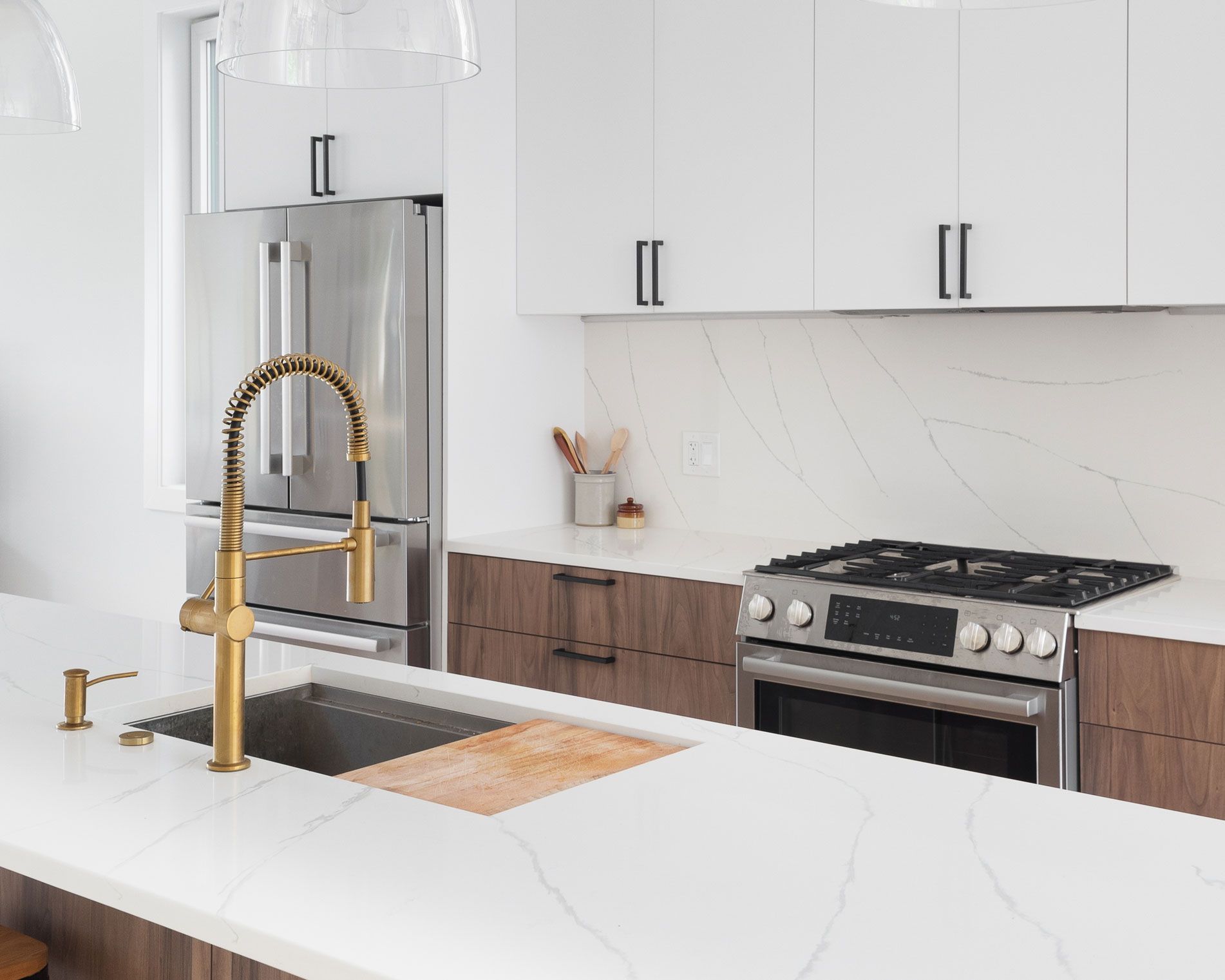 Modern kitchen with gold faucet, stainless steel appliances, and white countertops.