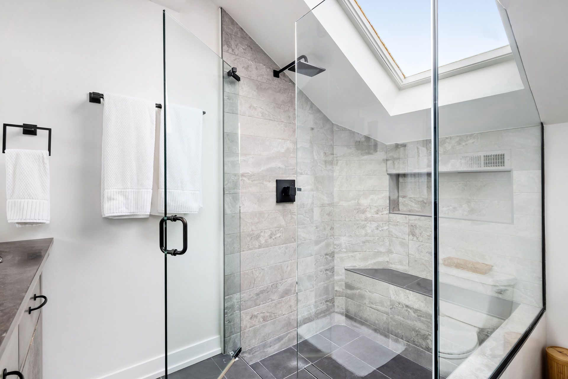 Modern bathroom with a glass-enclosed shower, white towels, and a skylight.