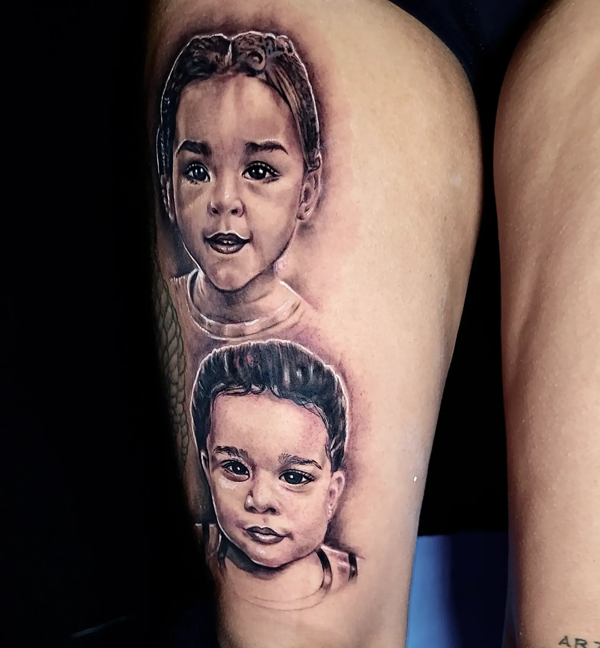 Un tatuaje de las caras de dos niños en la pierna de una persona.