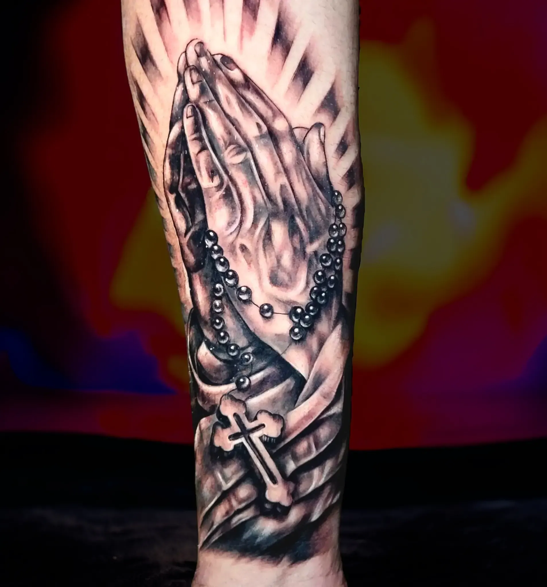 Un tatuaje de manos en oración con una cruz y un rosario.