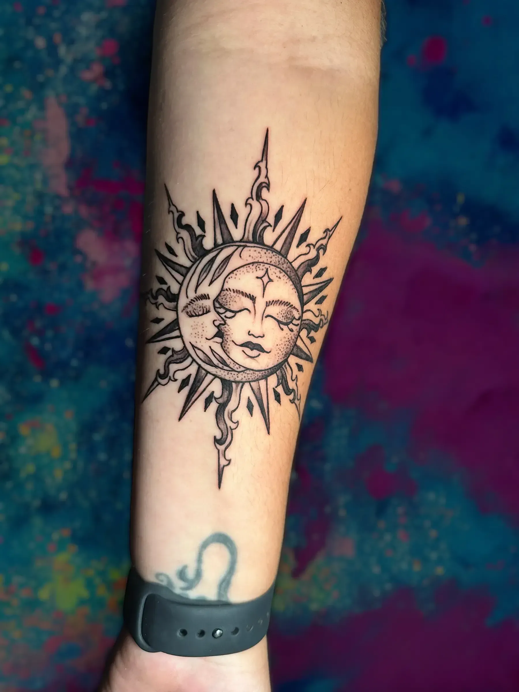 Una persona tiene un tatuaje de un sol con una cara en su antebrazo.
