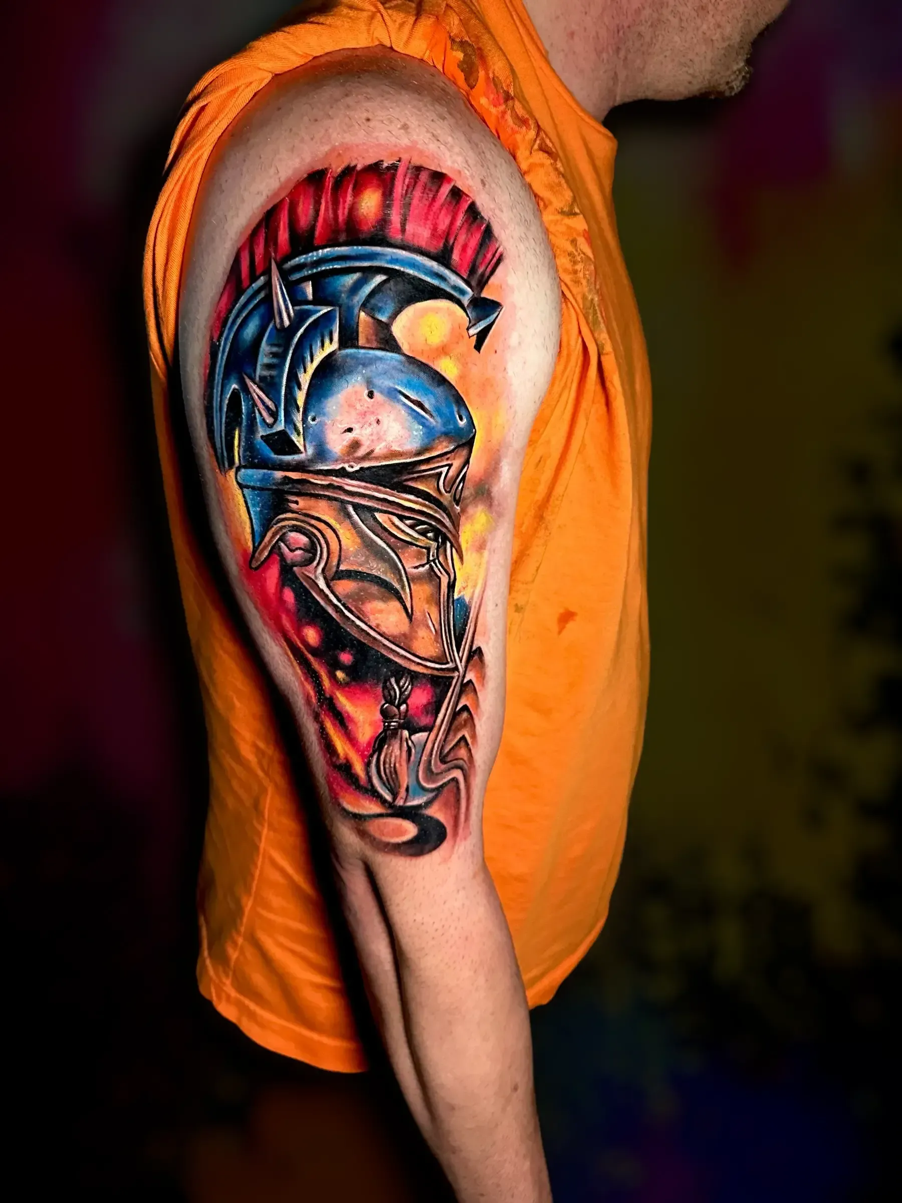 Un hombre con una camisa naranja tiene un tatuaje en el brazo.